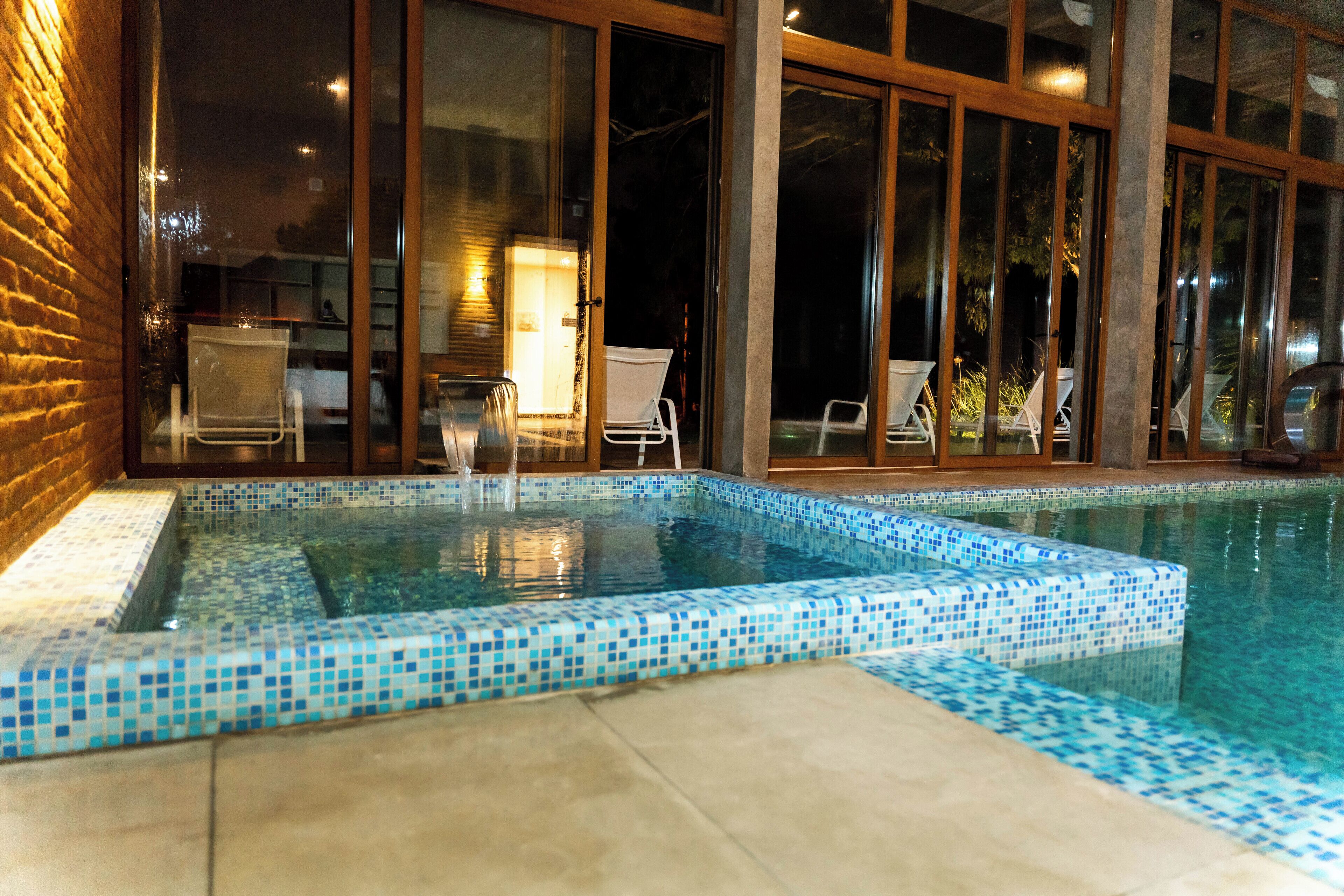 A swimming pool with a tiled edge, surrounded by glass doors and windows, and a brick wall on one side.