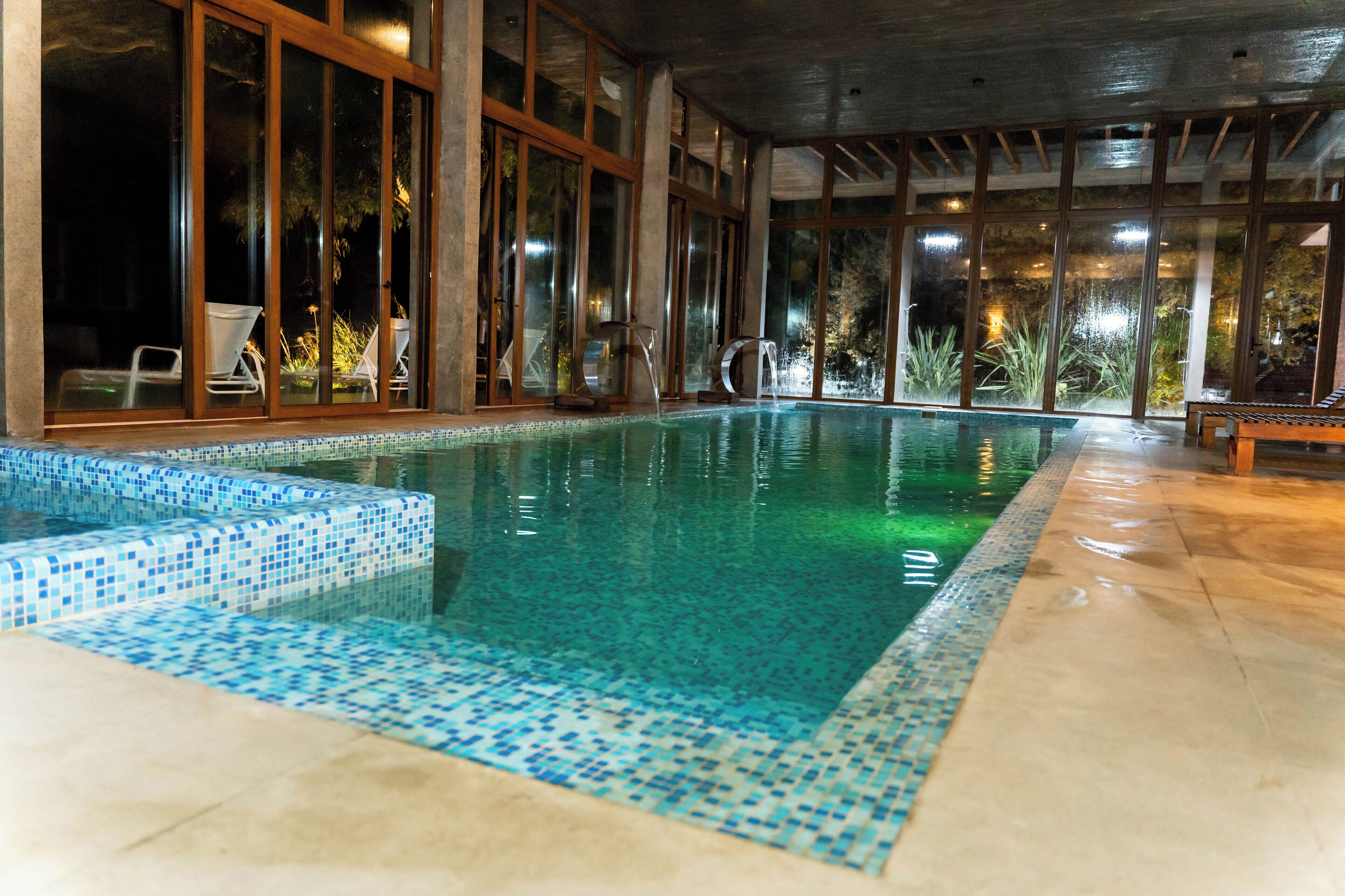 An indoor swimming pool with clear water, surrounded by large glass windows and wooden beams.