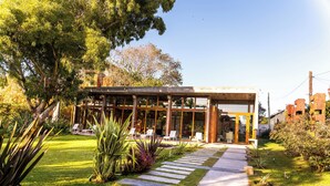 A modern building with a glass facade, a stone pathway leading to a seating area with chairs, and a well-maintained lawn. - O2 Hotel Valeria del Mar (Valeria del Mar)
