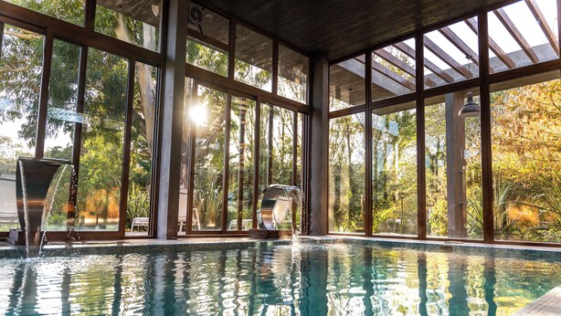 An indoor swimming pool with clear glass walls, a water fountain, and a view of trees outside. - O2 Hotel Valeria del Mar (Valeria del Mar)