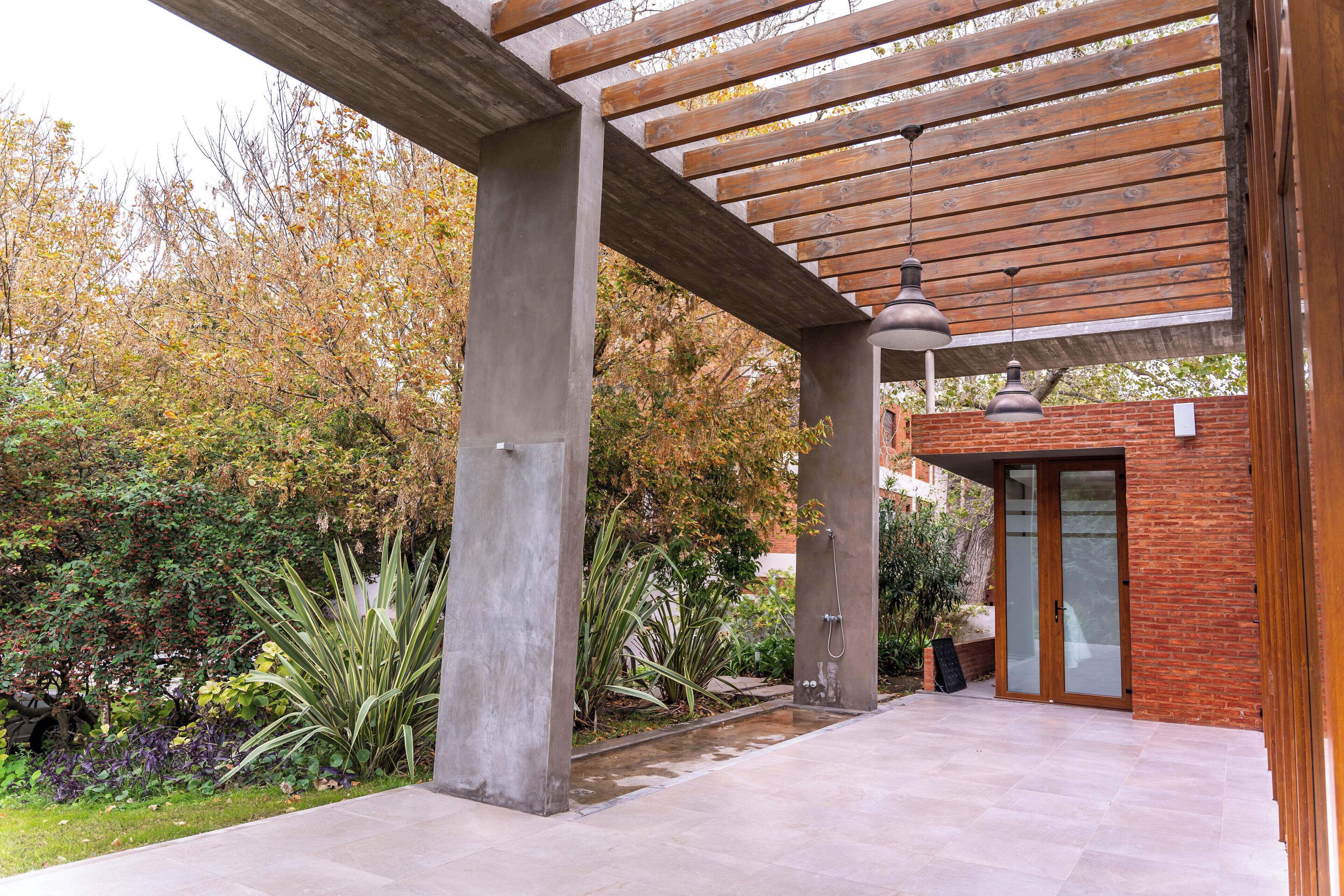 A covered outdoor area with a pergola, concrete pillars, and a brick wall.