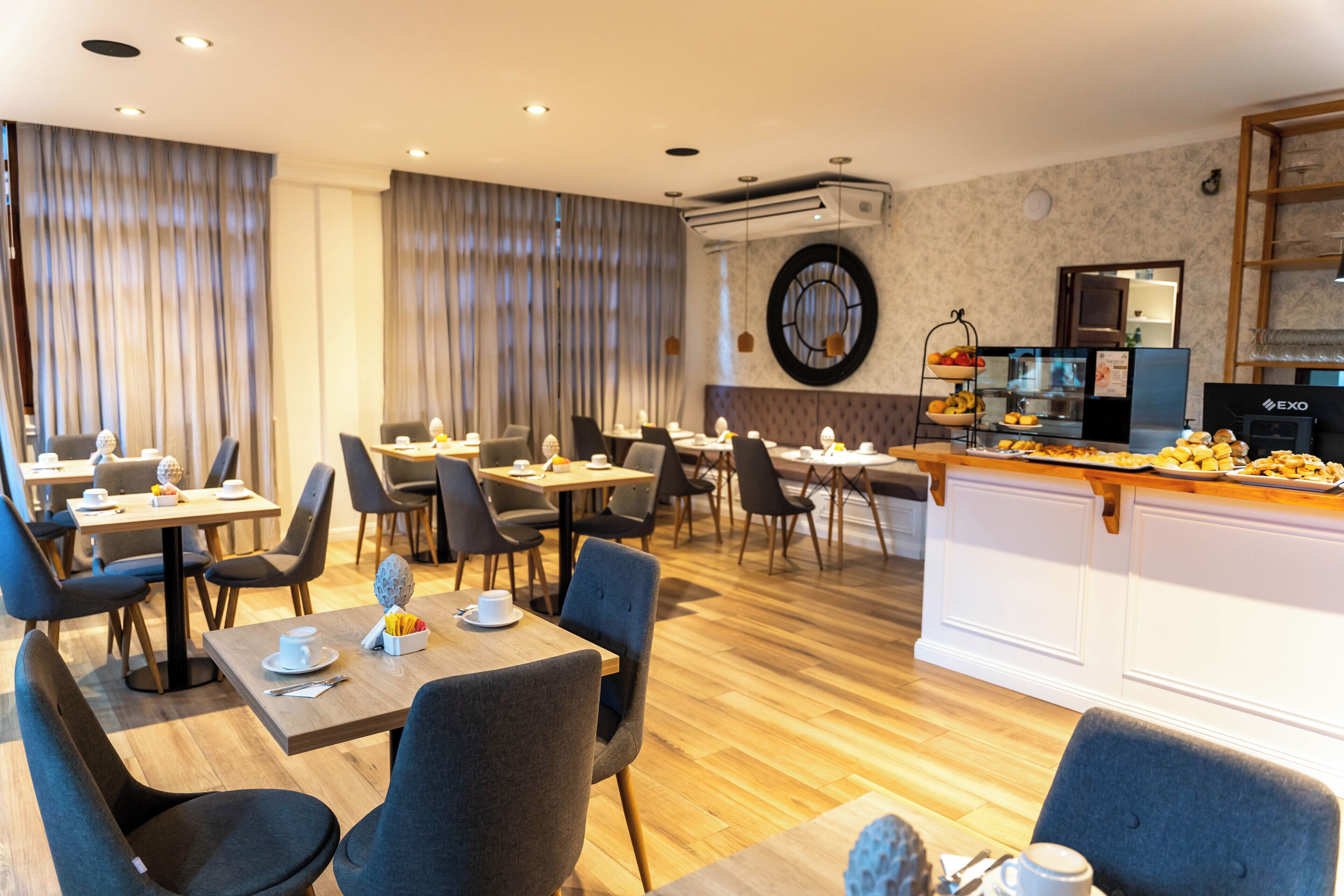 A modern dining area with wooden tables and chairs, a central buffet, and a kitchen area with a coffee machine.