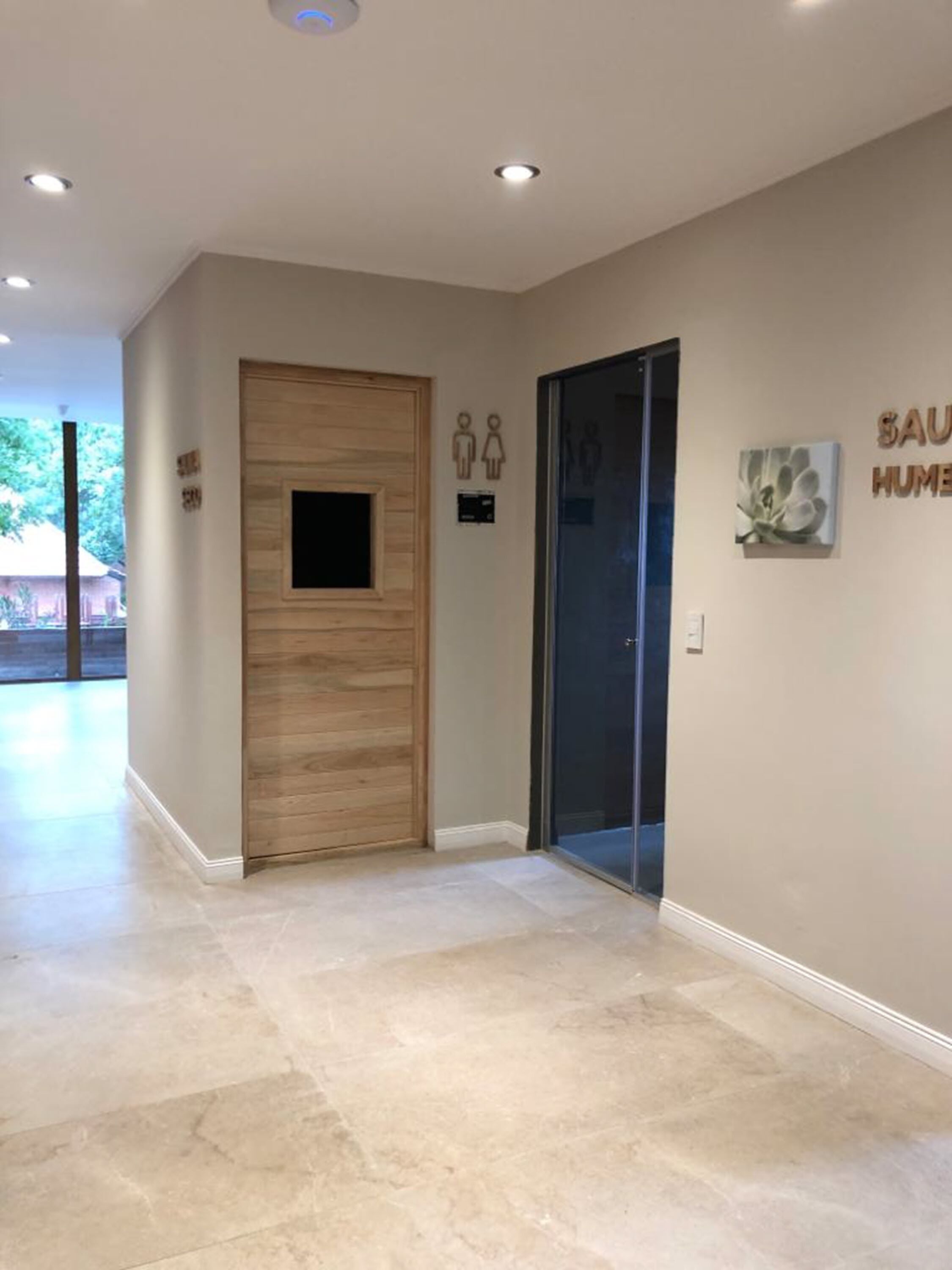 Un pasillo moderno con una puerta de madera, una puerta de cristal y un letrero que indica los baños de hombres y mujeres.