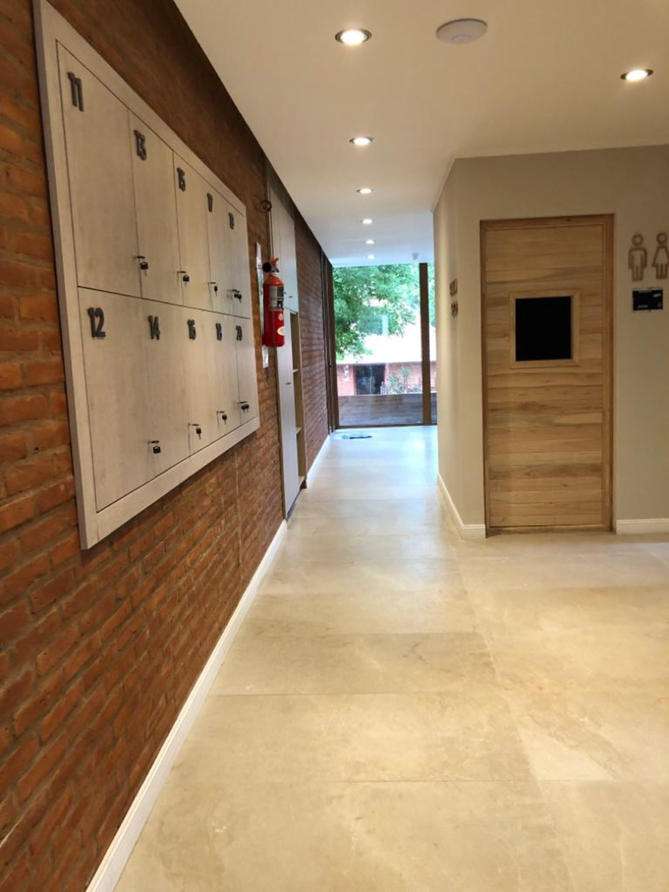 A hallway with lockers, a fire extinguisher, and a door with a peephole.
