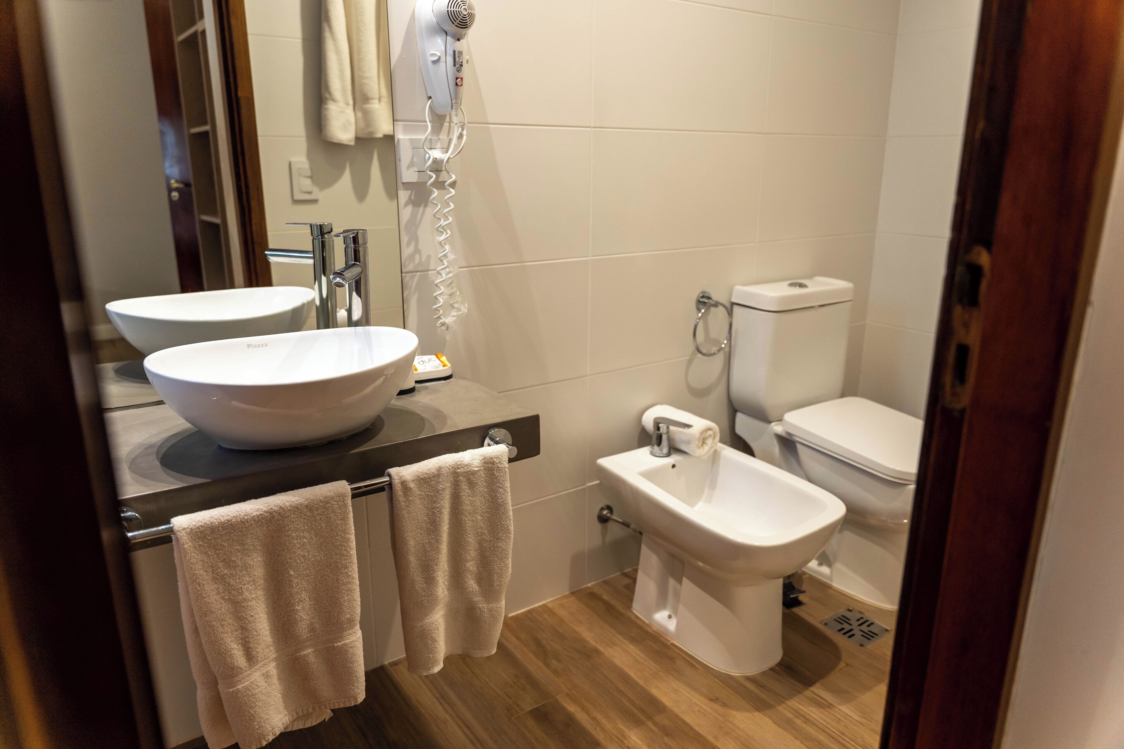 A modern bathroom with two sinks, a bidet, and a hairdryer mounted on the wall.