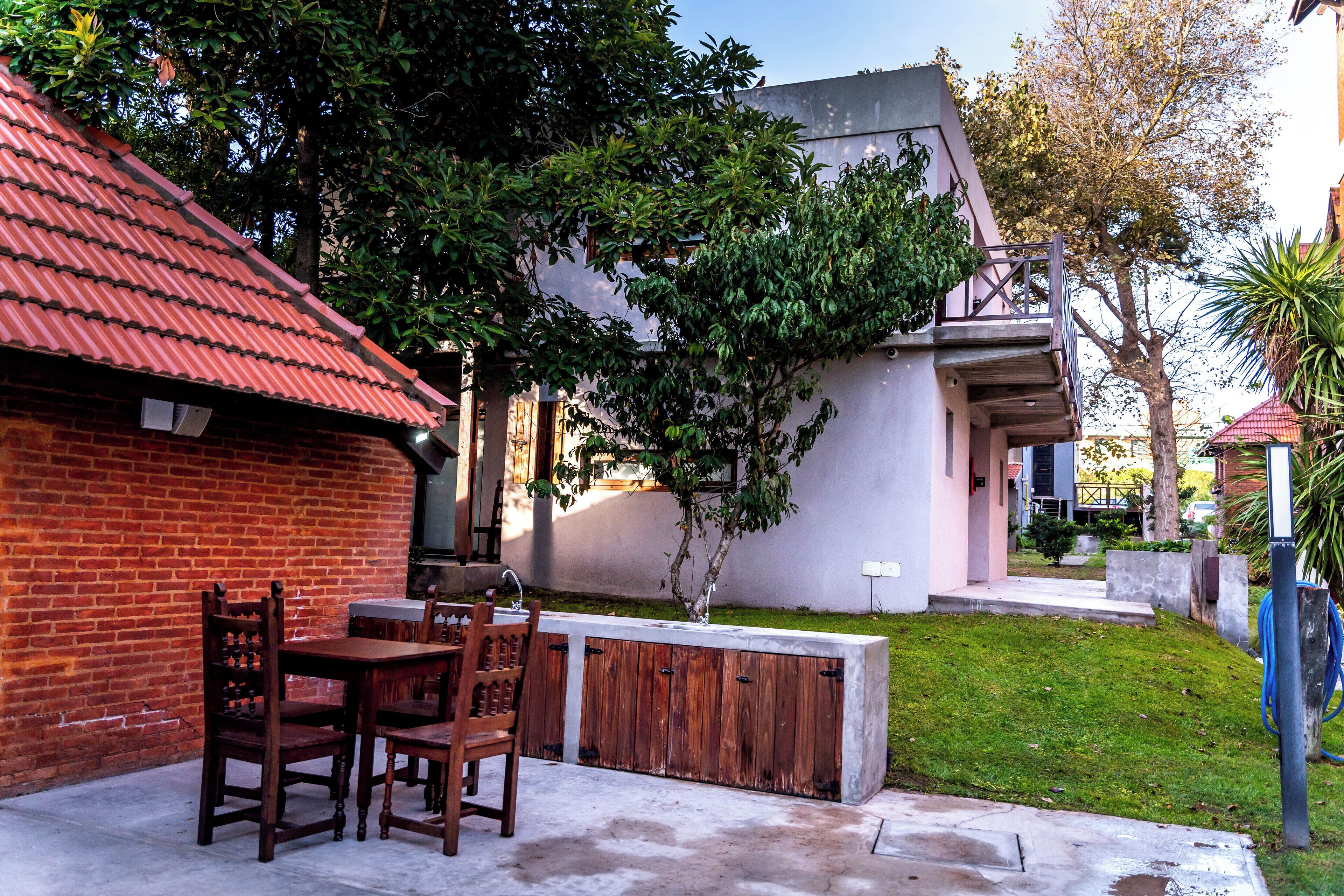A patio with a brick wall, a wooden table and chairs, and a small garden area with a tree and grass.