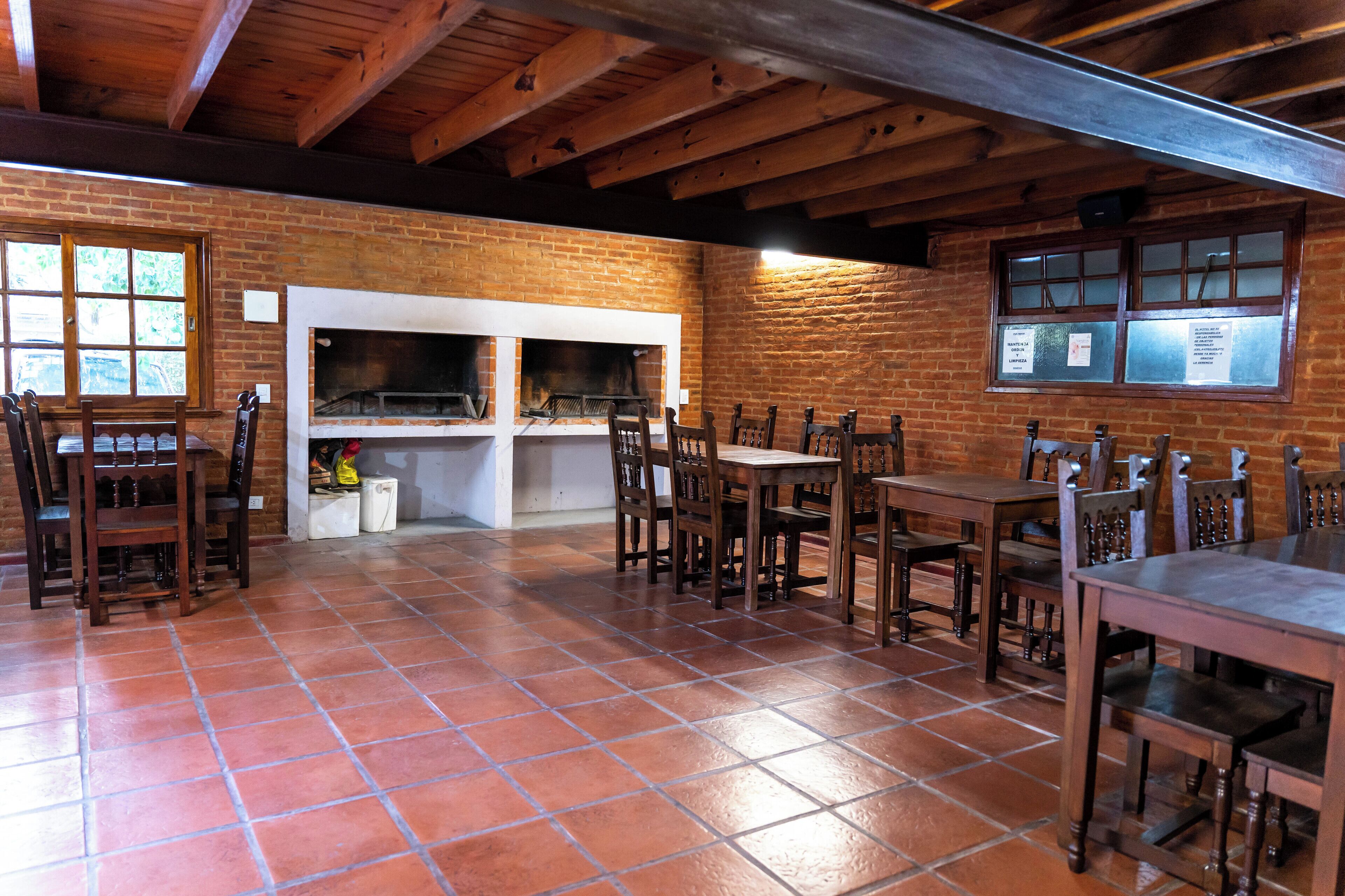 Un comedor rústico con paredes de ladrillo, mesas y sillas de madera, y piso de baldosas.