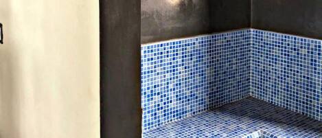 A corner of a room with a blue-tiled bench, a light fixture on the wall, and a framed picture.