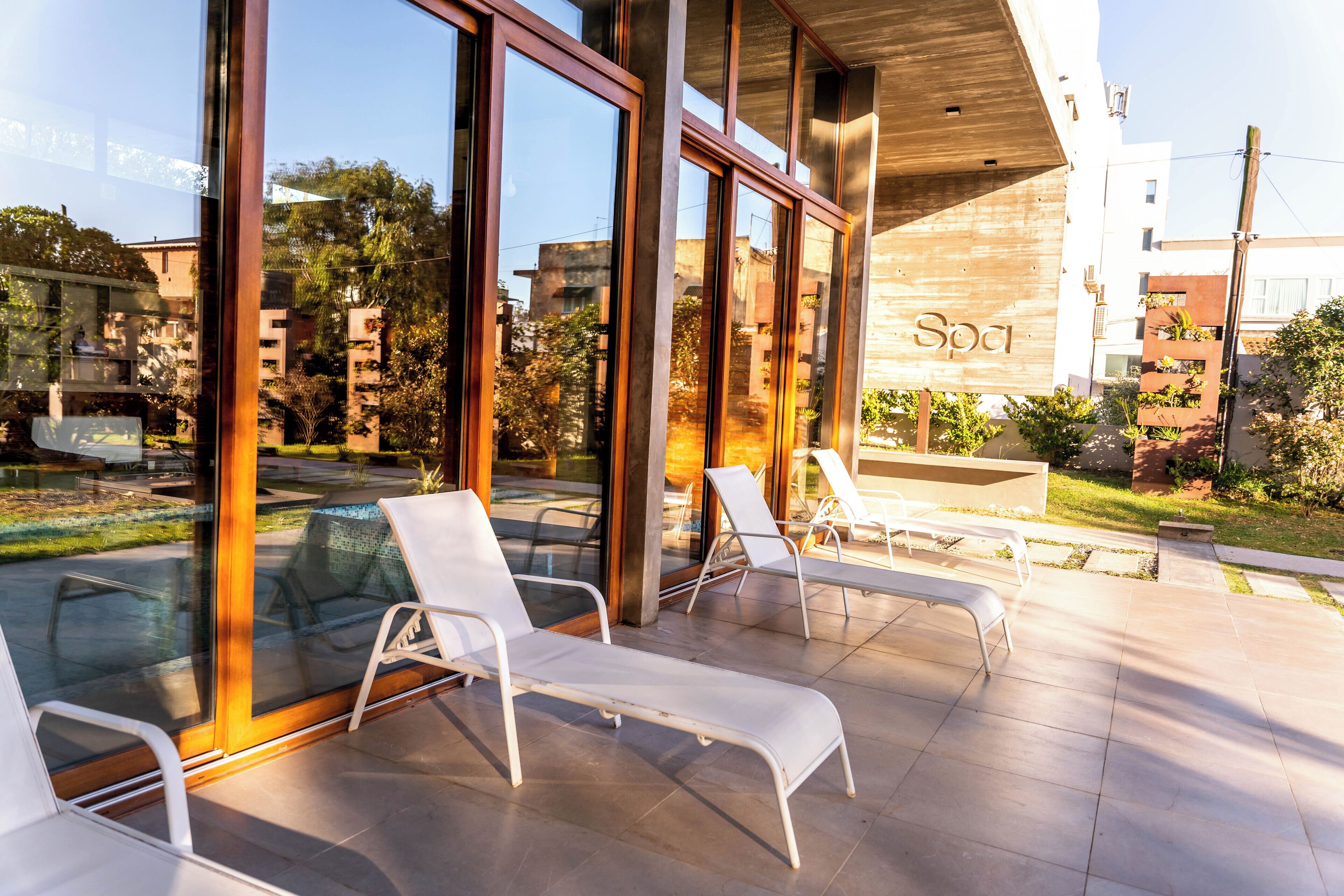 Ett modernt utomhusområde med loungekänsla, glasväggar, vita loungestolar och en pergola i trä.