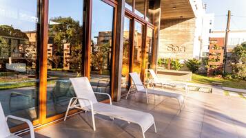 Ett modernt utomhusområde med loungekänsla, glasväggar, vita loungestolar och en pergola i trä.