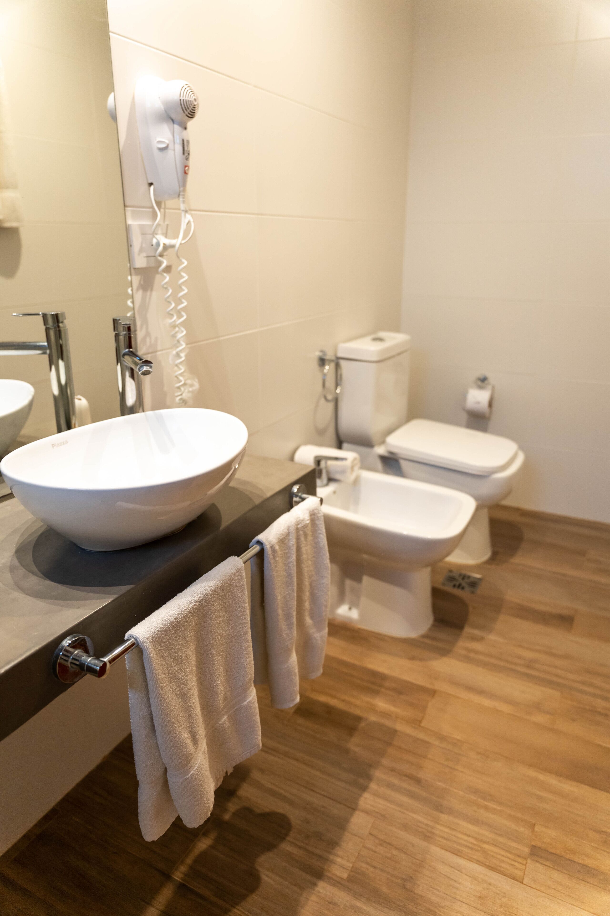 Un bany modern amb un gran mànec blanc, un vàter, un lavabo i un assecador de cabells fixat a la paret.