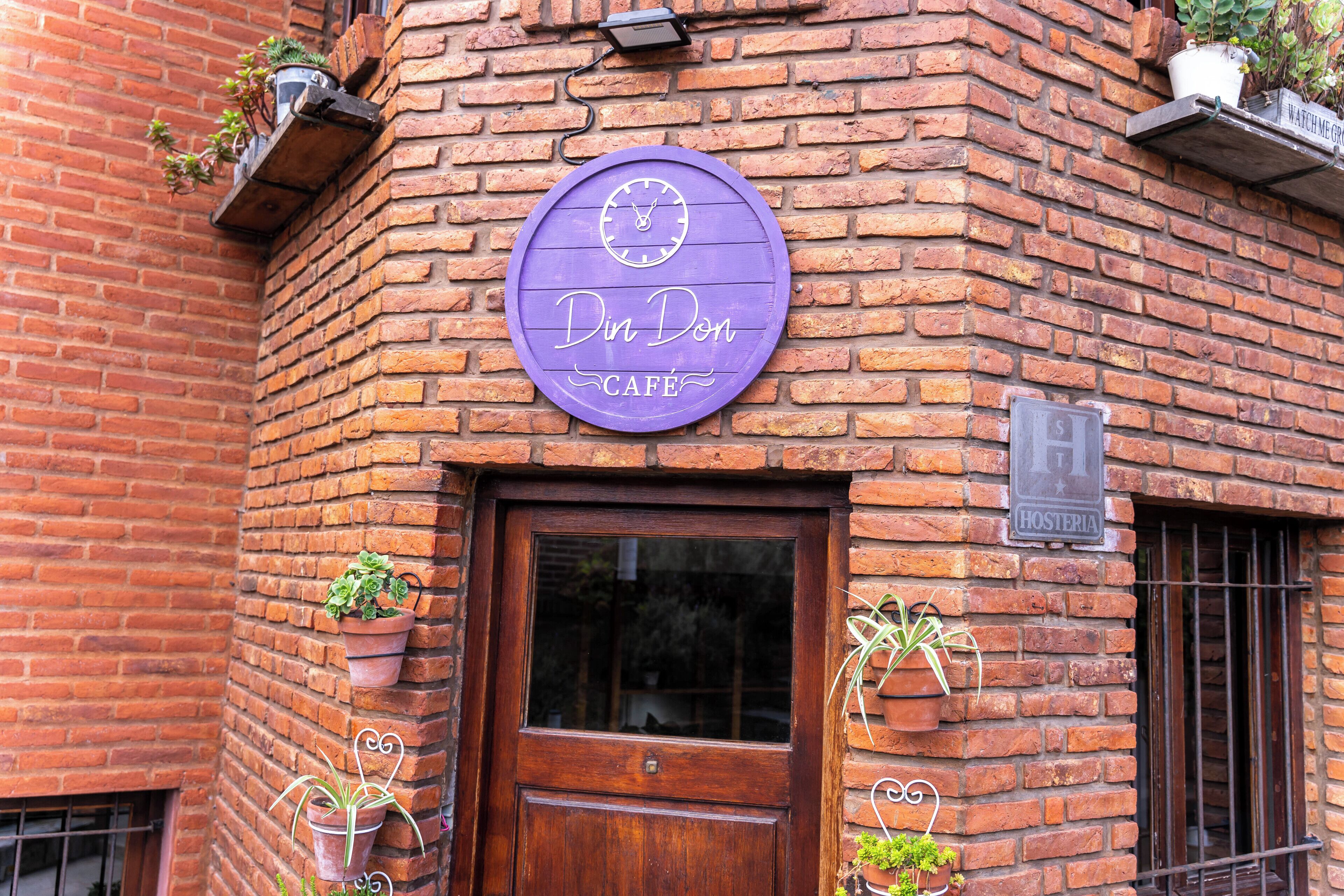A brick building with a wooden door and a purple sign that reads "Din Don Café".