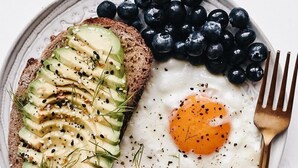 A plate with two sunny-side-up eggs, a slice of avocado toast, and a handful of blueberries. - Willow Pond Motel (Catskill)