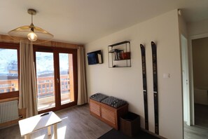 Una stanza con una scrivania in legno, una panca, un portasci e vista su un edificio attraverso un'ampia finestra.