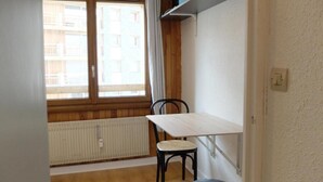 Um quarto pequeno com janela, radiador, mesa e cadeira.