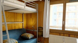 Quarto com beliche, colchão azul, almofadas xadrez, escada, radiador e janela com cortinas.