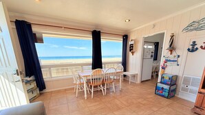 Ett rum med utsikt över stranden, ett matbord med stolar, en soffa och ett litet bord med dekorativa föremål.