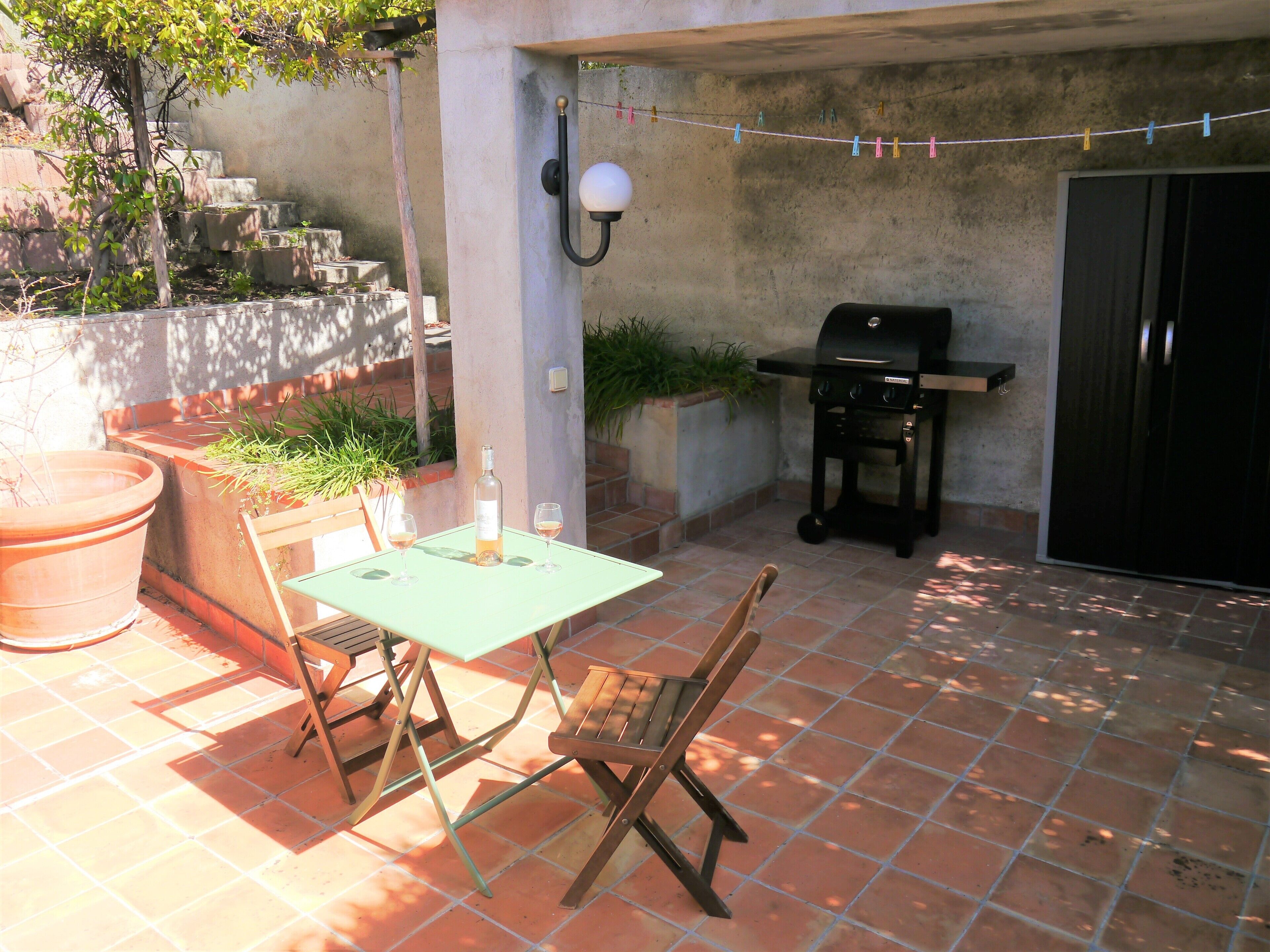 An outdoor patio with a table and chairs, a bottle of wine, and a grill.