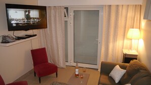 Olohuone, jossa on televisio, punainen nojatuoli, sohva, lasilla varustettu pöytä ja lamppu.