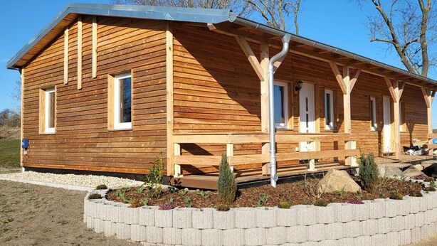 Eine Holzhütte mit Veranda, einem kleinen Garten und blauem Himmel.