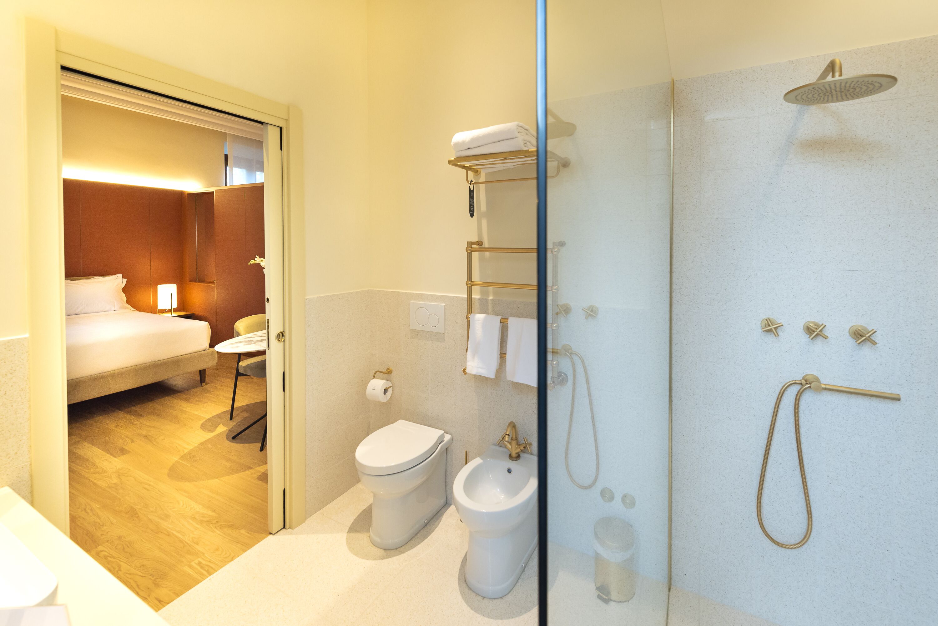 A modern bathroom with a shower, toilet, bidet, and a small bedside table with a chair.