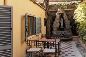 An outdoor patio with a stone fountain, a statue, and a table with chairs.