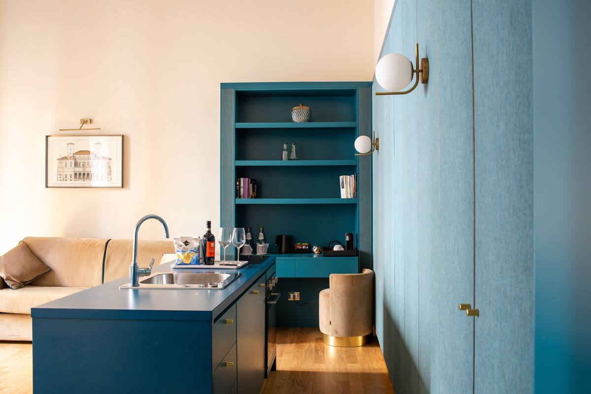 A compact kitchen with a blue countertop, a sink, and a beige chair.