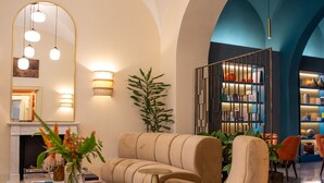 A modern living room with a beige sofa, a glass coffee table, and a large mirror. There is a fireplace in the background and a plant in the corner. - Sentho Roma (Rome)