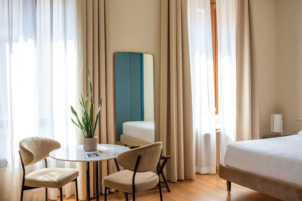 A hotel room with a bed, a round table with chairs, a potted plant, and a blue accent wall.