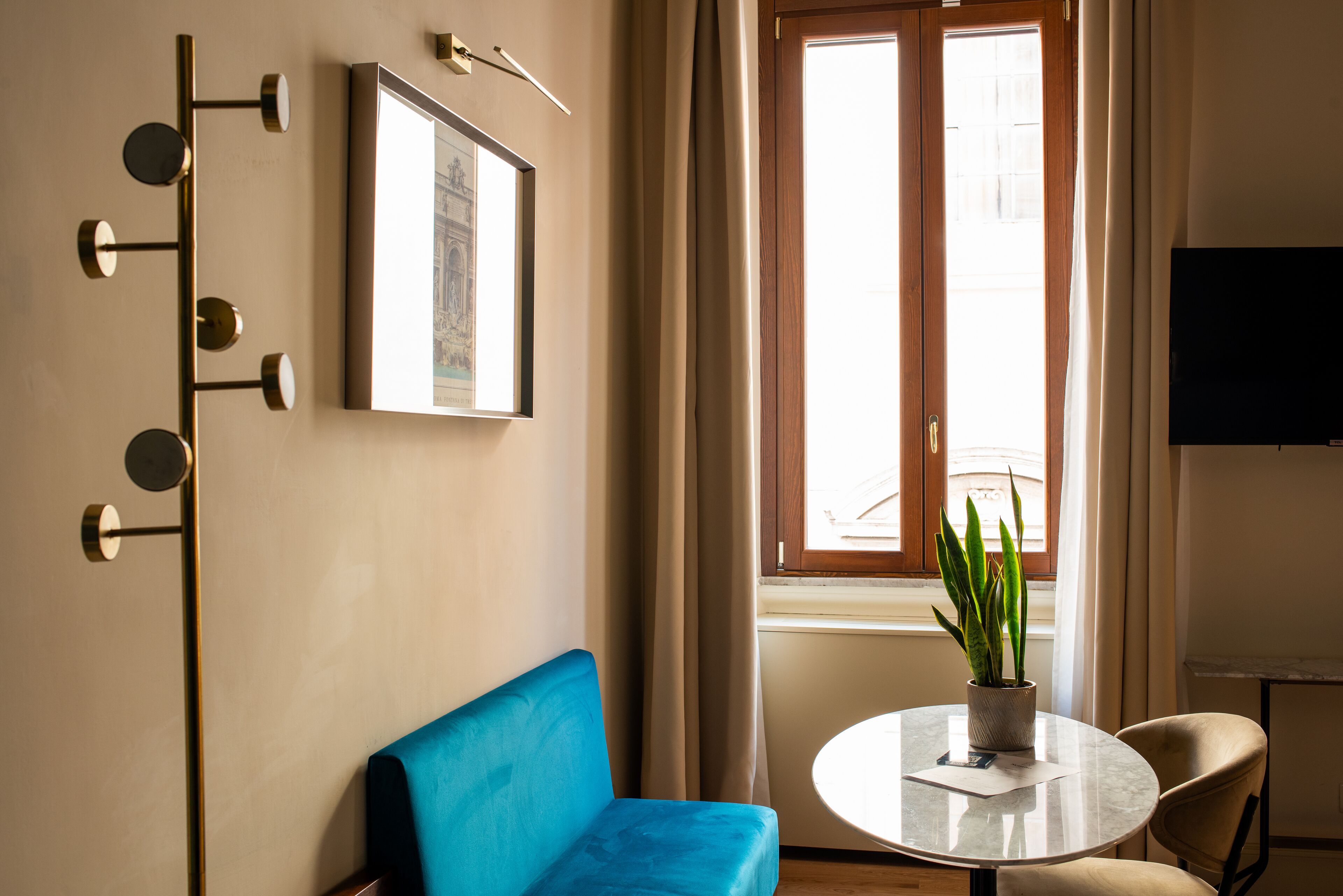 Una habitación moderna con un sofá azul, una mesa redonda con una planta en maceta, una lámpara de pared y un cuadro enmarcado.
