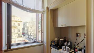 Une chambre d’hôtel avec une fenêtre donnant sur le paysage urbain, une kitchenette équipée d’une machine à café et un petit plan de travail sur lequel sont disposés divers objets.