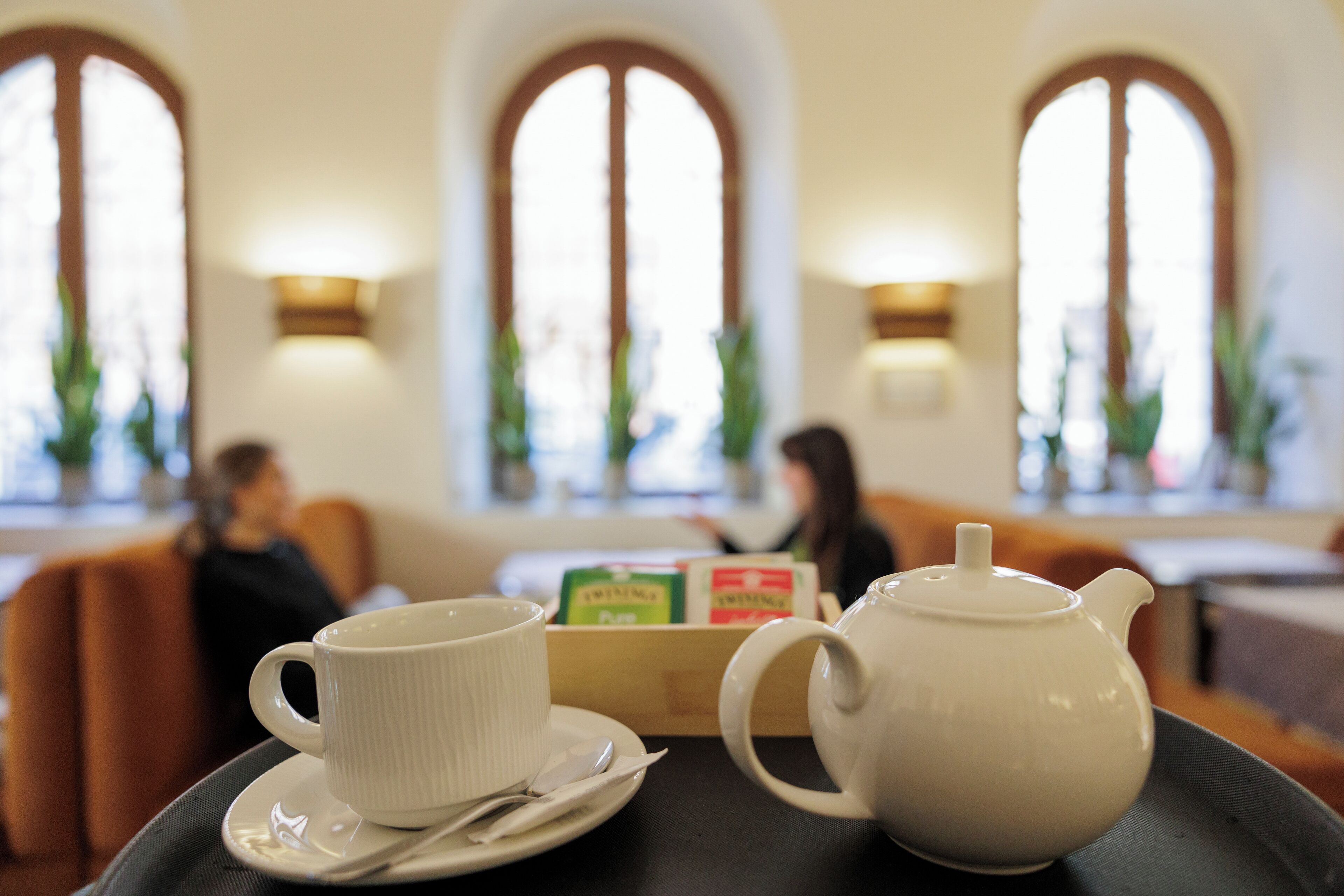 Ein Tisch mit Teekanne und Tasse, vor einer Kulisse aus Bogenfenstern und einer Sitzecke.