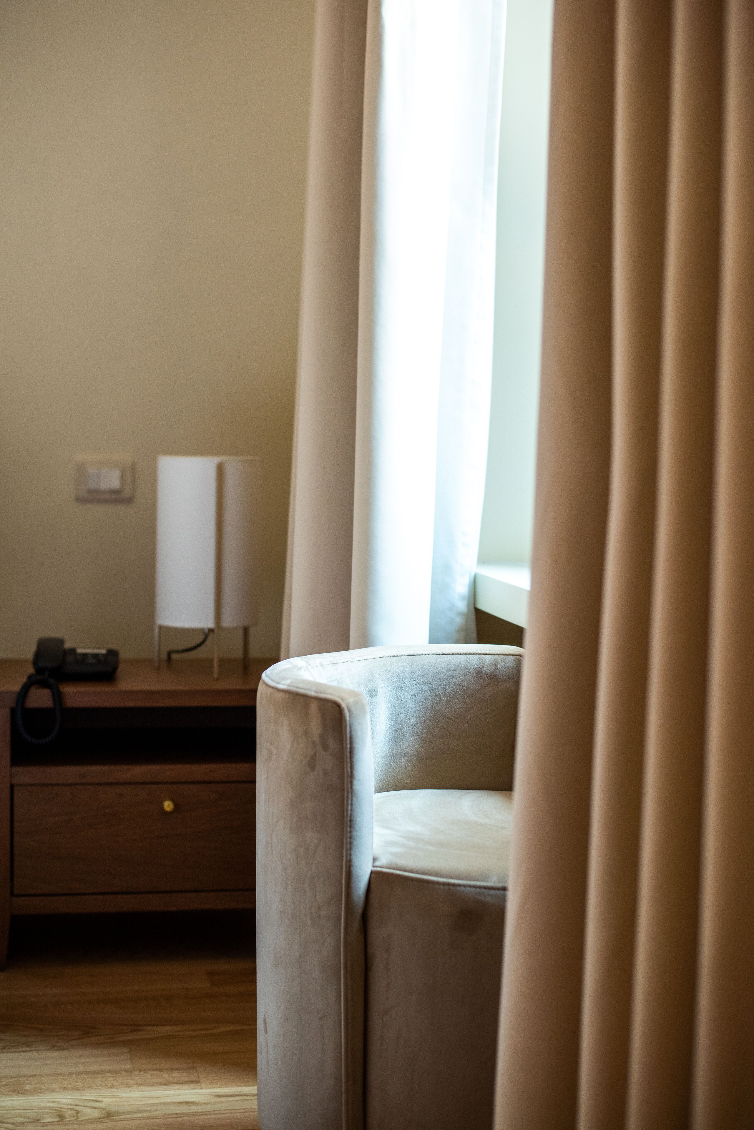 Ein Zimmer mit einem Holztisch, einer Lampe, einem Stuhl und einem Vorhangfenster.