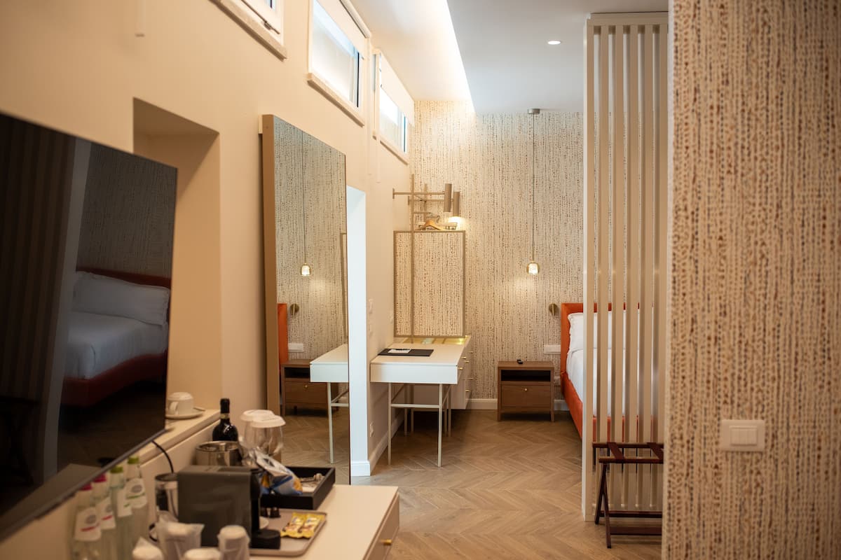 A hotel room with a bed, a desk, a mirror, a wardrobe, and a bathroom with a shower and toilet.