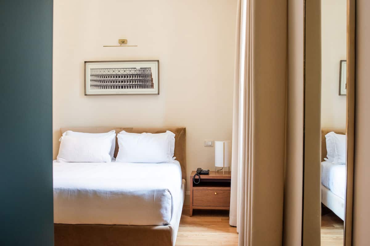 A hotel room with a bed, a nightstand, a lamp, and a framed picture on the wall.