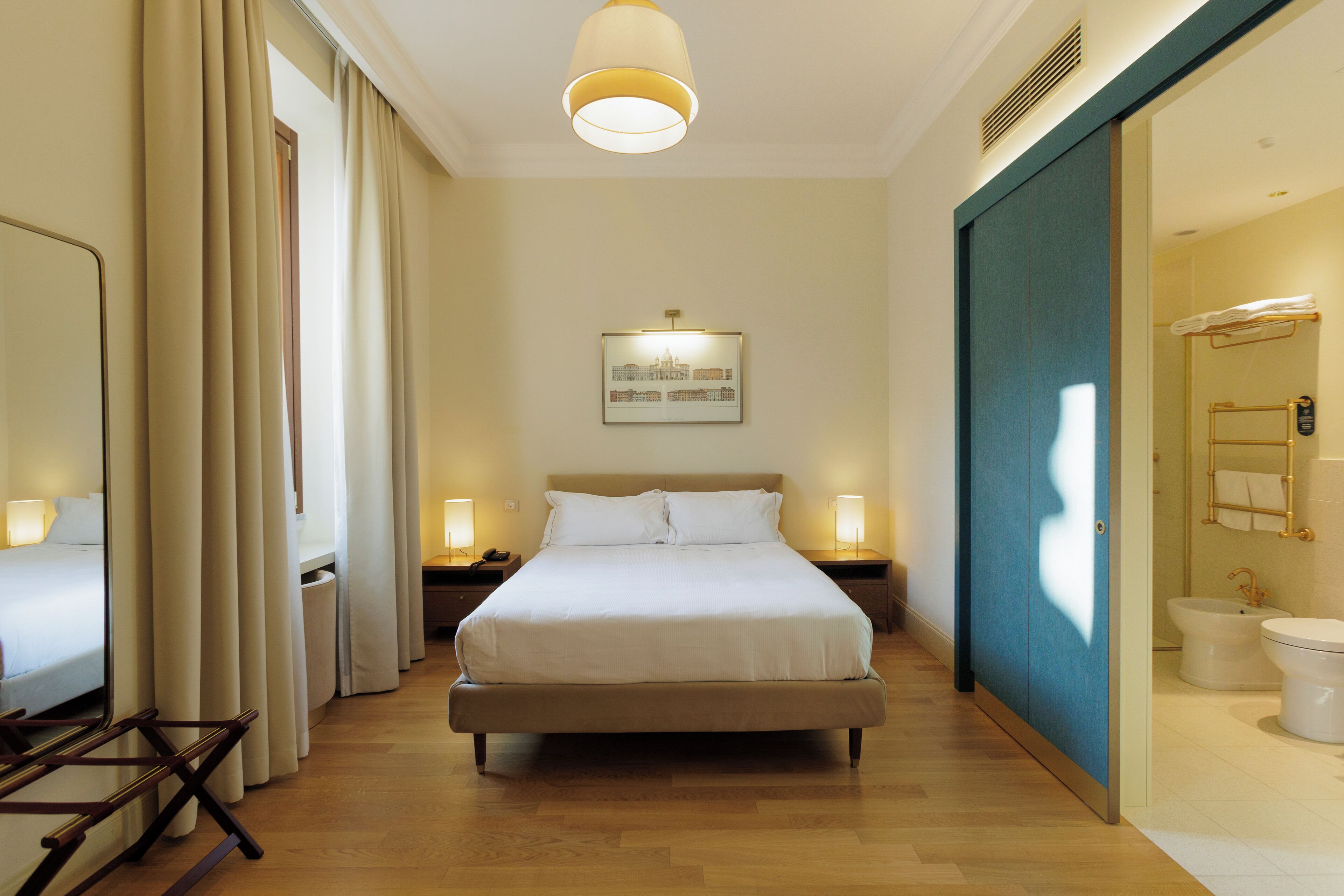 A hotel room with a large bed, bedside lamps, a framed picture on the wall, and a bathroom with a toilet and bidet.