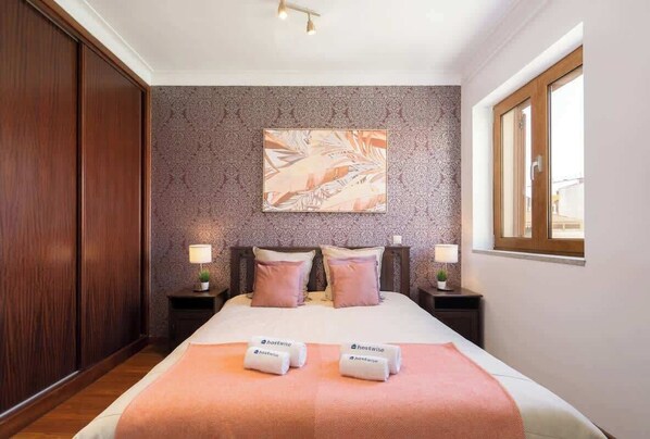 Une chambre d’hôtel avec un grand lit, deux tables de chevet avec des lampes, un tableau accroché au mur et une fenêtre.