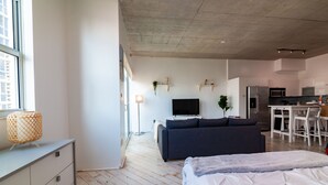 A modern apartment with a bed, sofa, kitchenette, and a large window. - Spacious studio apartment with a balcony (Miami)