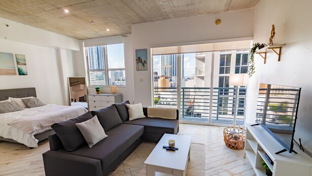 A modern living room with a sectional sofa, a small white coffee table, and a TV on a white stand. - Spacious studio apartment with a balcony (Miami)