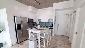 A modern kitchen with white cabinetry, a stainless steel refrigerator, a microwave, and a dining table with chairs. - Spacious studio apartment with a balcony (Miami)