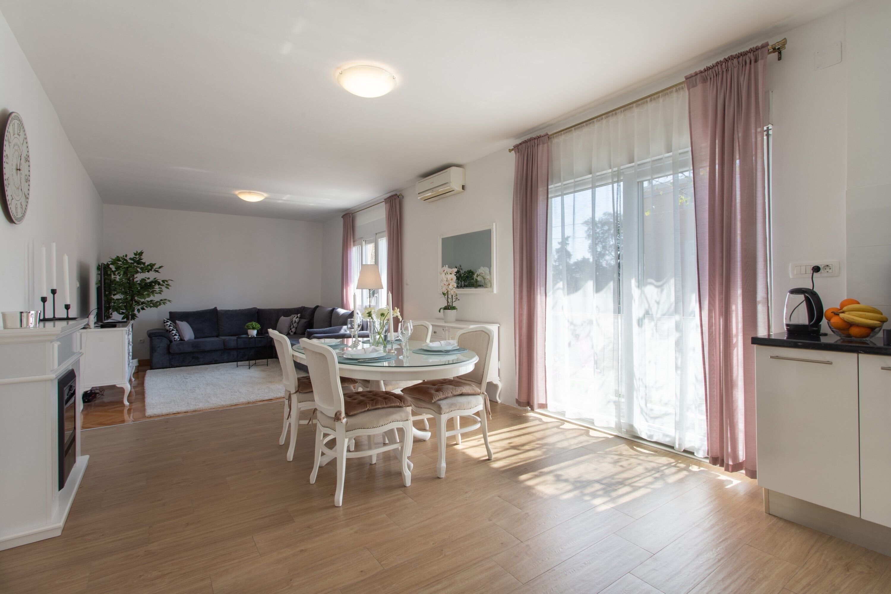 A modern living room with a dining area, featuring a round table, white chairs, and a sofa.
