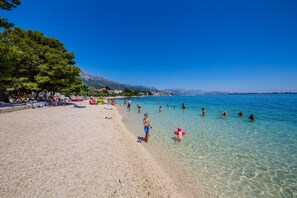 A beach with clear water, people swimming, and a mountain in the background.