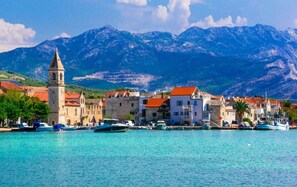 A coastal town with historic buildings, a prominent church tower, and boats docked along the waterfront.