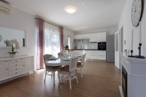 A modern kitchen with white cabinets, a dining table with chairs, and a large window with curtains.