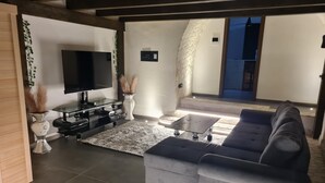 Una sala de estar moderna con un sofá seccional gris, un televisor de pantalla plana, una mesa de centro de vidrio y un jarrón decorativo con plumas de pampa.