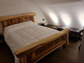 Ein Schlafzimmer mit einem Bettgestell aus Holz, weißer Bettwäsche, einem Nachttisch und einem kleinen Beistelltisch.