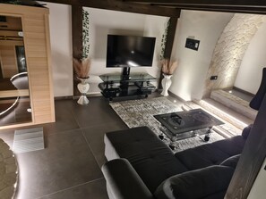 Ein modernes Wohnzimmer mit einem Flachbildfernseher, dunklen Sofas, einem Glastisch und dekorativen Vasen.