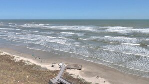 Una playa con un paseo marítimo de madera que conduce a un edificio con fachada de vidrio.