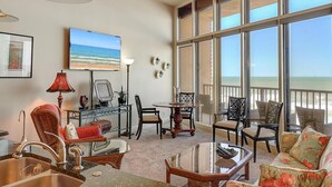 Amplia sala de estar con un gran ventanal con vistas a la playa, comedor con mesa redonda y asientos cómodos.