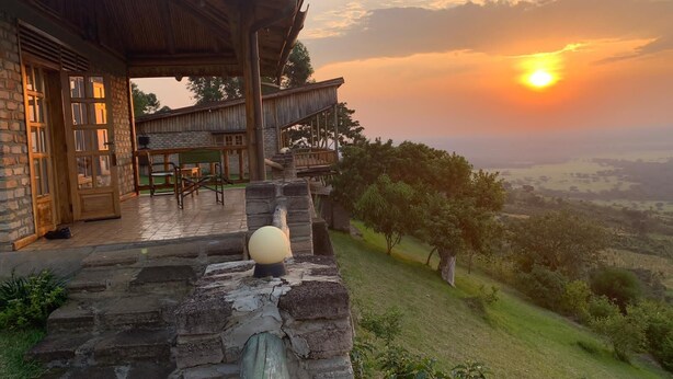 A stone staircase leading to a wooden deck with a view of a sunset over a hilly landscape. - Rift Valley Game Lodge (Rubirizi)